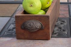 a wooden box filled with green apples on top of a tile floor