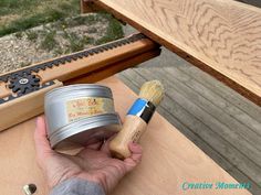 a person holding a paintbrush and some tins on a table