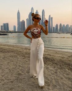 a woman standing on top of a sandy beach next to the ocean and tall buildings