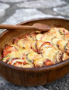 a wooden bowl filled with food on top of a stone floor next to a wooden spoon