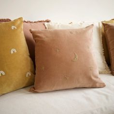 four pillows on a white couch with gold stars and crescents embroidered on them, all in different colors