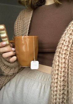 a woman holding a coffee cup and cell phone in her right hand while sitting down