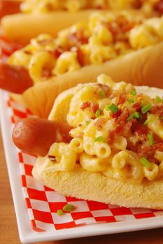 two hotdogs with macaroni and cheese on them are sitting on a red and white checkered plate