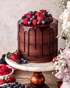 a chocolate cake with fresh berries and blueberries on the top is surrounded by flowers