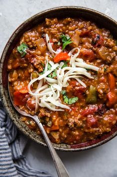 a bowl filled with chili and noodles on top of a white table cloth next to a spoon