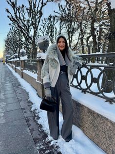 a woman standing in the snow next to a fence