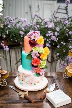 a multi - tiered cake with colorful flowers on the top is sitting on a table