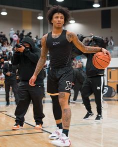 a man holding a basketball while standing on top of a gym floor with other people in the background