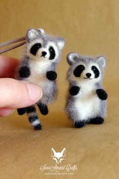 two tiny raccoon figurines are being held by a person's finger