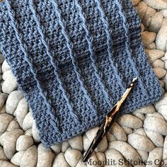 a pair of scissors laying on top of a knitted blue blanket next to rocks