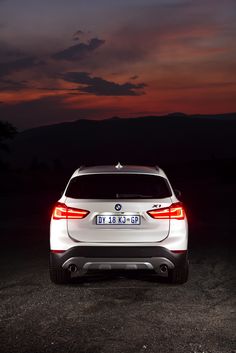 the back end of a white car parked on top of a dirt field at night