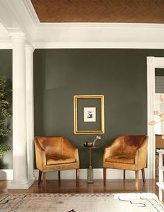 two brown chairs sitting next to each other on top of a hard wood floor in front of a green wall