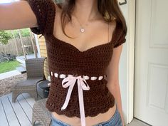 a woman wearing a brown crochet top with a pink ribbon around her waist