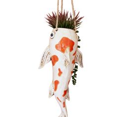 an orange and white fish hanging from a rope with spiky hair on it's head