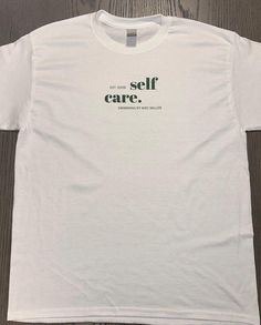 a white t - shirt with the words self care printed on it, sitting on a wooden floor