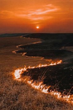 the sun is setting over an open field with grass and fire coming out of it