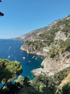 boats are floating in the blue water next to a rocky cliff and trees on either side