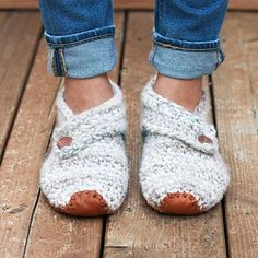 the feet of a person wearing crochet slippers on a wooden floor with blue jeans