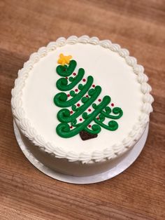 a white cake decorated with green icing and a christmas tree on the top is sitting on a wooden table