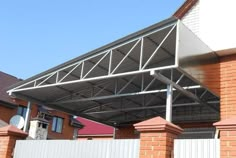 a large metal roof on top of a red brick building next to a white fence