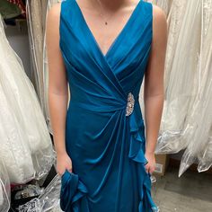 a woman in a blue dress looking at her cell phone while standing next to some dresses