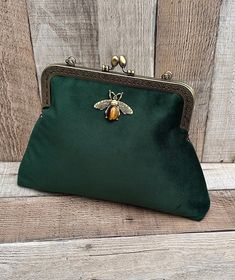 Stunning, handmade, velvet clutch bag with bee detail. The lining is made with a beautiful floral cotton fabric. Use it as a classic clutch or attach the shoulder strap to wear over your shoulder or as a crossbody - Bronze colour Chain strap (detachable) - Bronze colour Kiss lock clasp - H: 18.5cm x W: 26.5 x D: 4cm approximately - Metal clasp width: 18cm - Tiger eye stone detail (The markings on the stone may be slightly different ) - Tassel Due to different monitor settings, colours may differ slightly from those pictured More green handbags available here: https://www.etsy.com/uk/listing/1610033489/ https://www.etsy.com/uk/listing/1435806192/ https://www.etsy.com/uk/listing/1209932037/ Satchel Clutch With Detachable Strap As Gift, Clutch With Detachable Strap Satchel Shape For Gift, Handheld Clutch With Detachable Strap For Gifts, Green Crossbody Clutch As Gift, Elegant Shoulder Bag With Zipper Pouch For Gifts, Elegant Shoulder Bag With Zipper Pouch As Gift, Detachable Strap Clutch Pouch As Gift, Elegant Handheld Shoulder Bag With Zipper Pouch, Crossbody Coin Purse As Gift