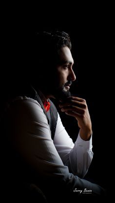 a man in white shirt and red bow tie holding something up to his face with dark background