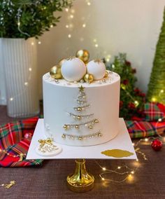 a white cake decorated with gold ornaments and baubles on a table next to christmas trees