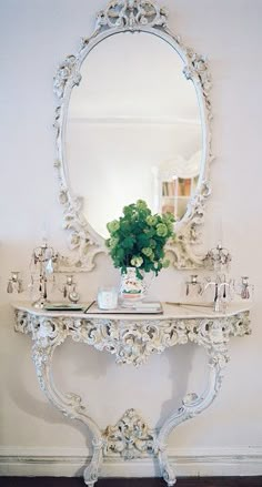 a white table with a mirror and vase on it