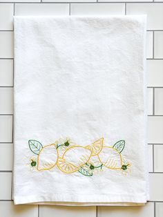 a white towel with lemons and leaves embroidered on it hanging from a tiled wall