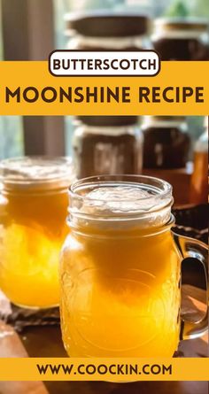 two mason jars filled with yellow liquid sitting on top of a table next to a window