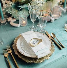 the table is set with gold and white plates, silverware, napkins, and candles