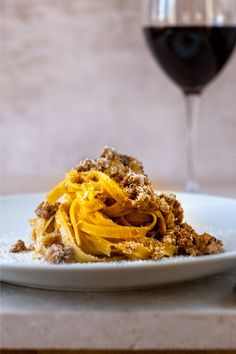 a white plate topped with pasta next to a glass of wine