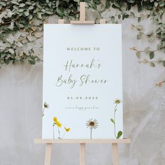 a welcome sign for a baby shower with daisies and greenery on the wall