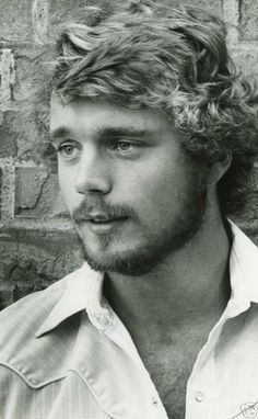 a black and white photo of a man with curly hair in front of a brick wall