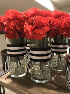 red carnations are in vases with black and white stripes on them, along with candy