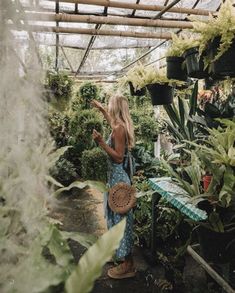 a woman standing in a greenhouse looking at plants and holding a straw hat on her head