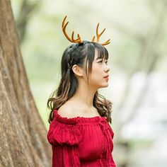 a woman with antlers on her head standing next to a tree