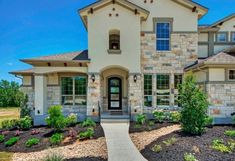 a large home with stone and stucco exterior, front door and entry way leading into the yard