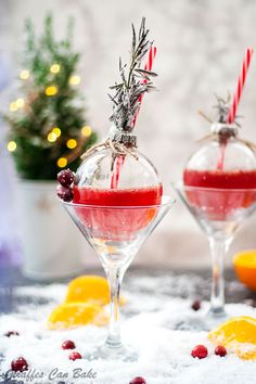 two wine glasses filled with red liquid and garnished with candy canes sitting on top of snow