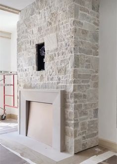 a room with a stone fireplace in the middle and white paint on the wall behind it