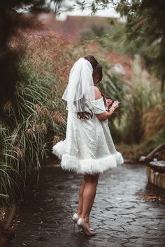 a woman in a white dress and veil is standing on a path with her phone