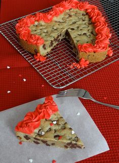 a cookie cake with red frosting and sprinkles sits on a cooling rack