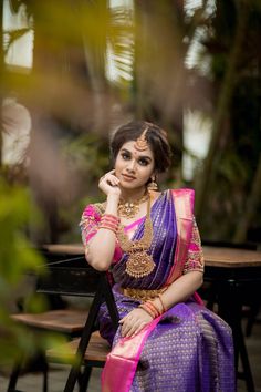 a woman in a purple and pink sari sitting at a table with her hand on her chin