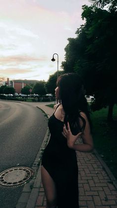 a woman in a black dress is walking down the street with her hand on her hip