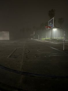 an empty basketball court at night with the lights on and fog in the air above