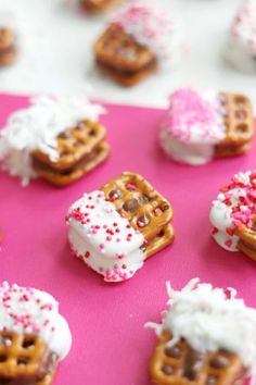 some pretzels are decorated with sprinkles and white frosting on a pink surface