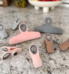 several pink and grey paper clips sitting on top of a marble counter next to a bowl of fruit