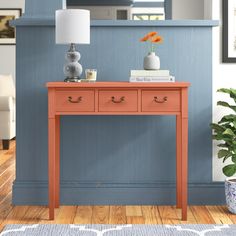 an orange table with two drawers in front of a blue wall and potted plant