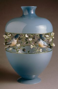 a blue vase with birds and flowers on the bottom is shown in front of a brown background